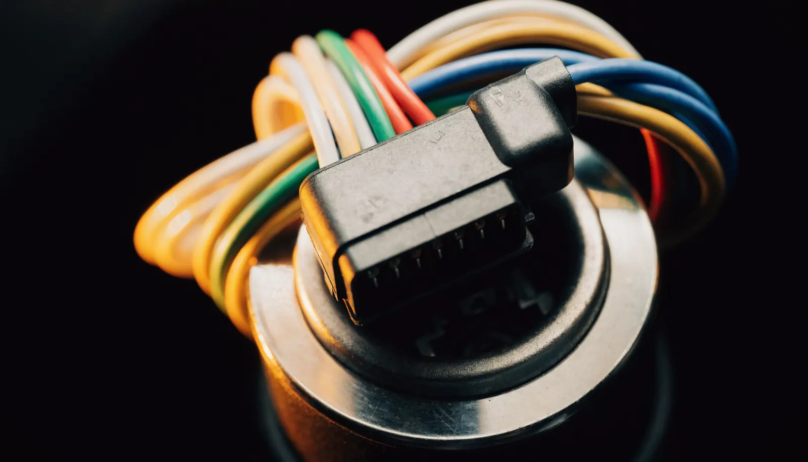 A diagnostic connector plugged into a vehicle OBD port with a loom of coloured wires behind it