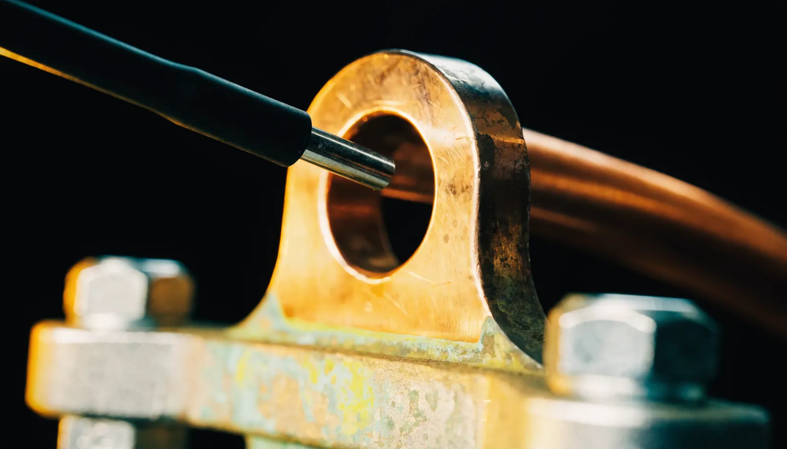 A multimeter probe touching a heavy copper earth lug bolted to a vehicle chassis